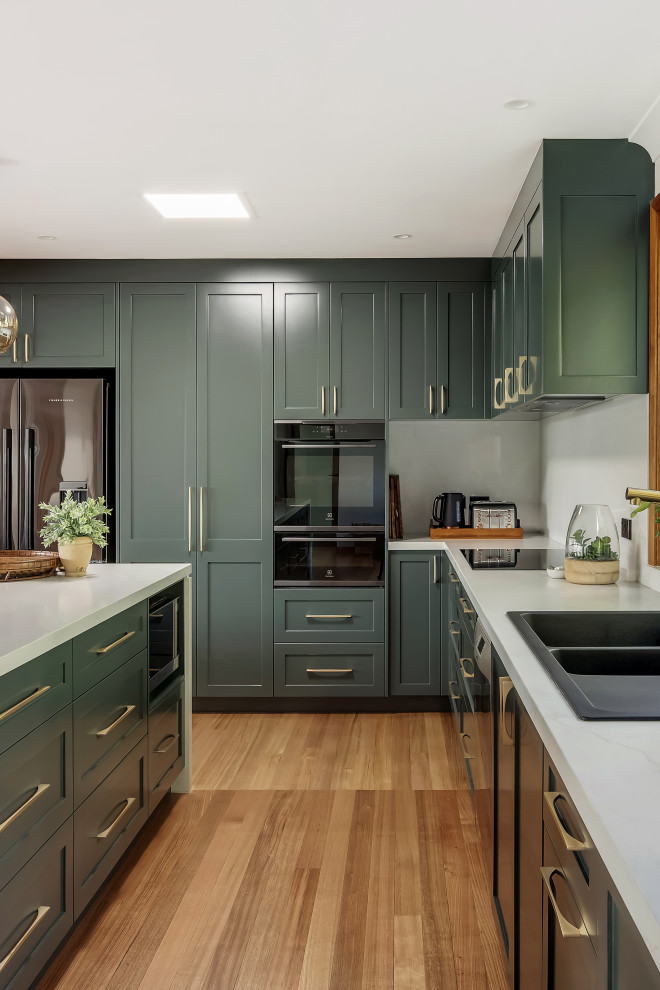 Example of a large transitional l-shaped medium tone wood floor and multicolored floor eat-in kitchen design in Sydney with a drop-in sink, shaker cabinets, green cabinets, quartz countertops, white backsplash, quartz backsplash, black appliances, an island and white countertops