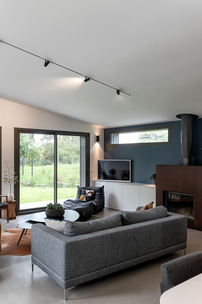 Cette image montre une très grande salle de séjour design ouverte avec un mur blanc, sol en béton ciré, un poêle à bois, un manteau de cheminée en métal, un téléviseur indépendant, un sol gris et éclairage.