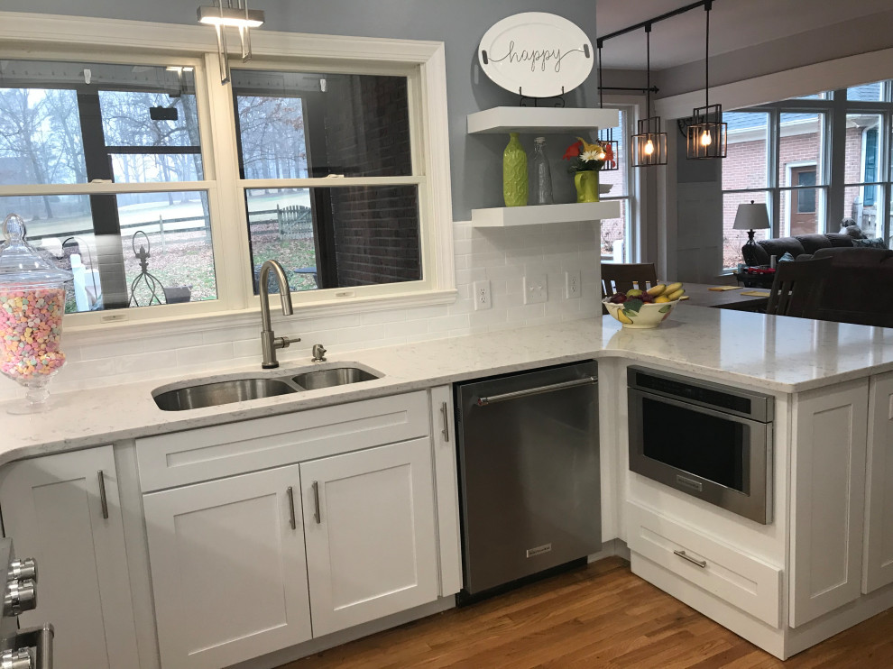Example of a mid-sized transitional u-shaped medium tone wood floor kitchen design in Charlotte with an undermount sink, shaker cabinets, white cabinets, quartz countertops, white backsplash, subway tile backsplash, stainless steel appliances and a peninsula