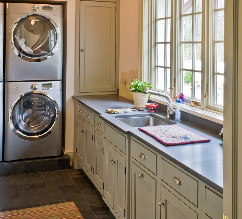 Photo of a mid-sized traditional l-shaped laundry room in Chicago with beaded inset cabinets, grey cabinets, soapstone benchtops, beige walls, slate floors, a stacked washer and dryer and an undermount sink.