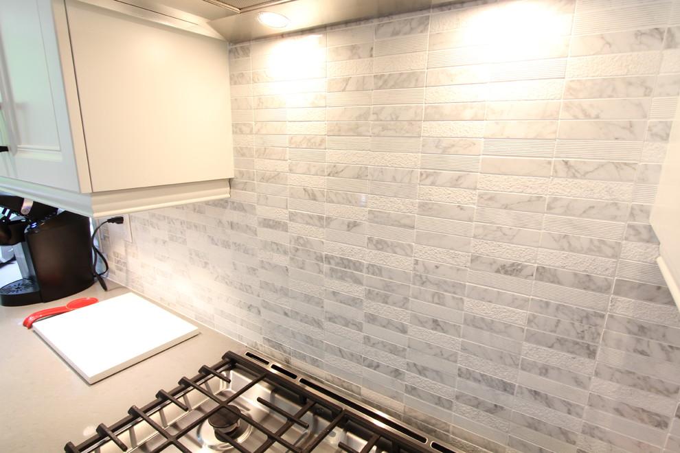 This is an example of a mid-sized transitional l-shaped eat-in kitchen in Toronto with an undermount sink, recessed-panel cabinets, white cabinets, quartzite benchtops, white splashback, mosaic tile splashback, stainless steel appliances, laminate floors and with island.