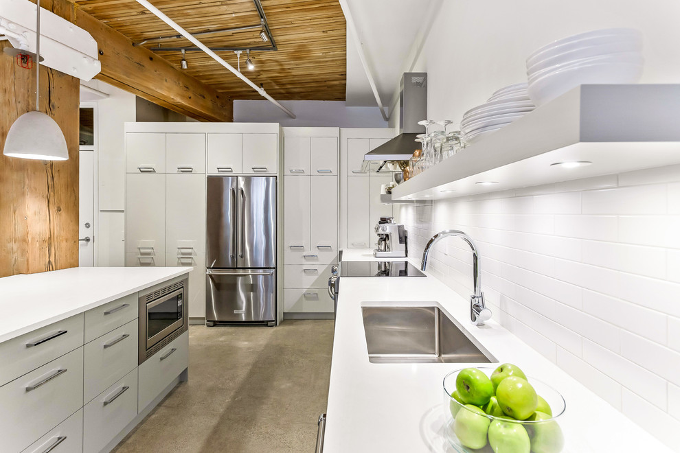 This is an example of an industrial u-shaped separate kitchen in Calgary with a single-bowl sink, flat-panel cabinets, grey cabinets, white splashback, brick splashback, stainless steel appliances, concrete floors, with island, grey floor and white benchtop.