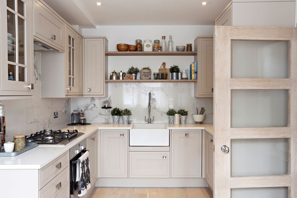 Inspiration for a small transitional u-shaped separate kitchen in London with a farmhouse sink, shaker cabinets, grey cabinets, white splashback, stainless steel appliances, light hardwood floors and no island.
