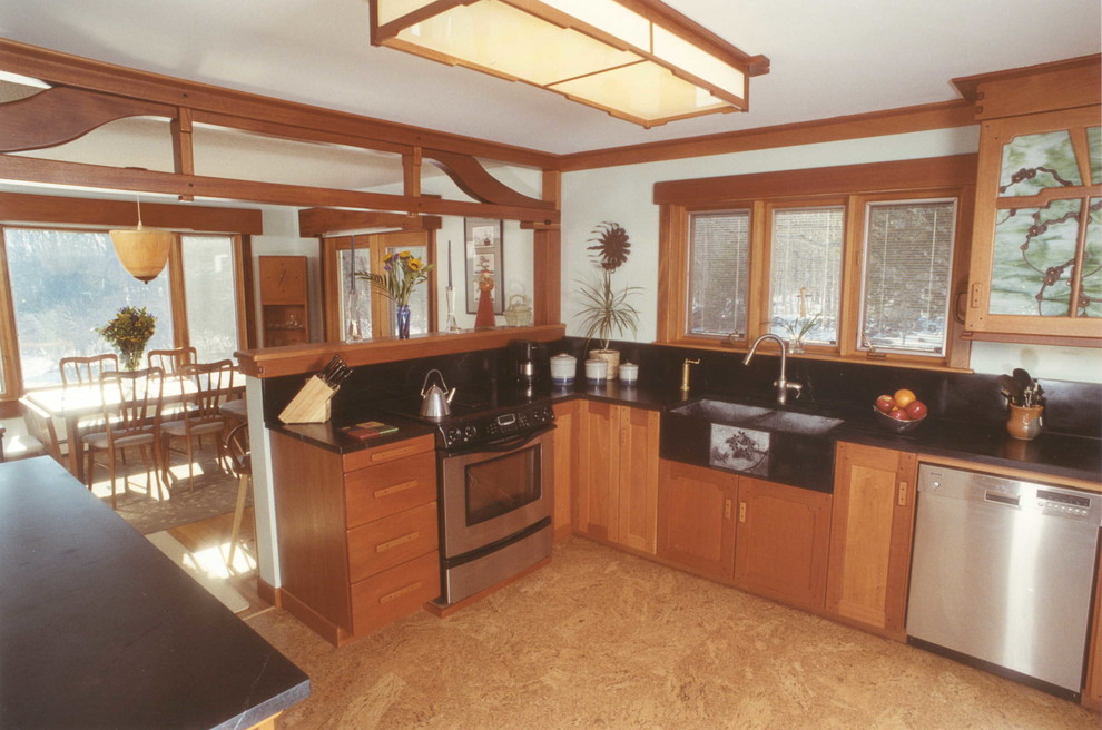 Photo of a mid-sized arts and crafts l-shaped eat-in kitchen in Boston with flat-panel cabinets, medium wood cabinets, soapstone benchtops, stainless steel appliances, a farmhouse sink and cork floors.