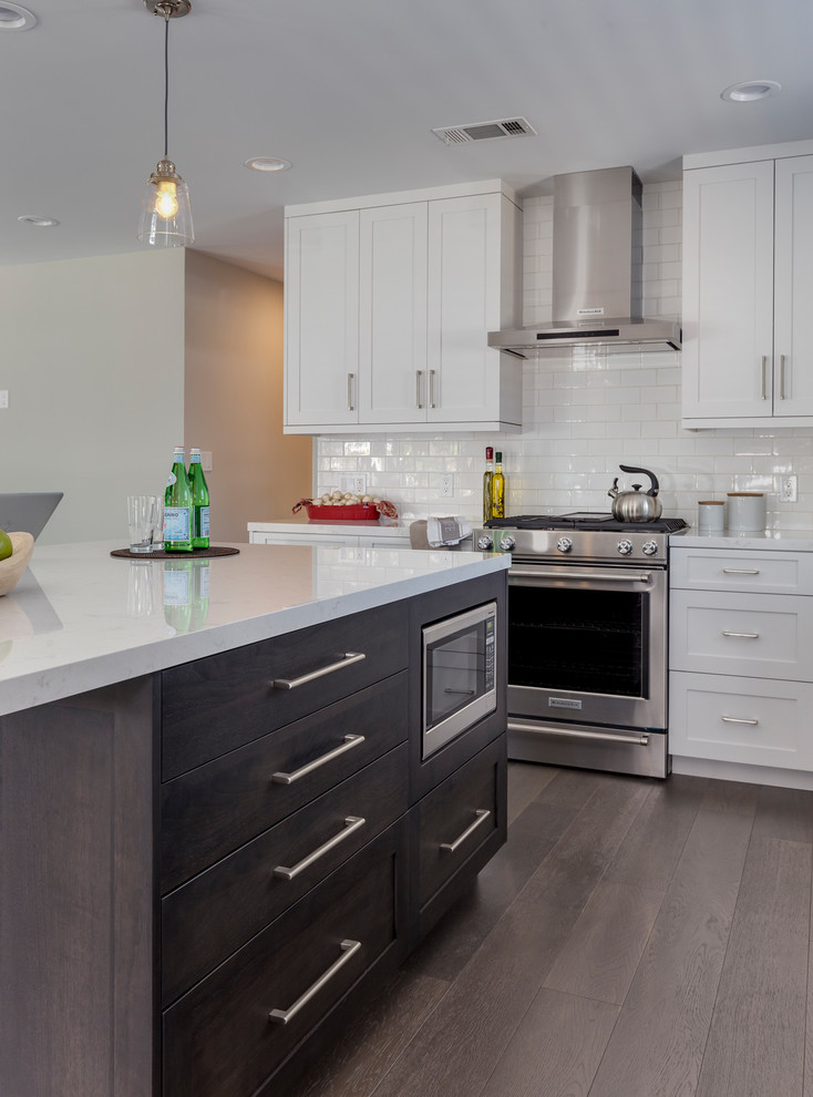 This is an example of a mid-sized transitional l-shaped open plan kitchen in Los Angeles with an undermount sink, shaker cabinets, white cabinets, quartz benchtops, white splashback, subway tile splashback, stainless steel appliances, dark hardwood floors, with island and brown floor.