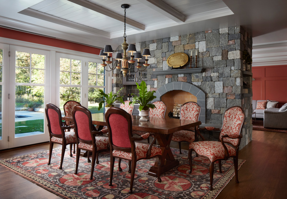 На фото: кухня-столовая в классическом стиле с темным паркетным полом, двусторонним камином, фасадом камина из камня, коричневым полом, многоуровневым потолком, панелями на части стены и розовыми стенами с