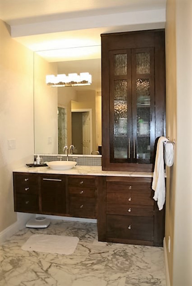 Design ideas for a large transitional master bathroom in Las Vegas with glass-front cabinets, dark wood cabinets, a drop-in tub, a double shower, a one-piece toilet, gray tile, stone tile, beige walls, marble floors, a vessel sink and marble benchtops.