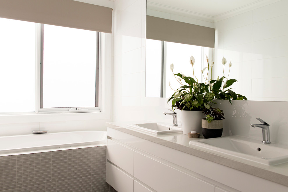 This is an example of a mid-sized contemporary master bathroom in Melbourne with a drop-in tub, a corner shower, a wall-mount toilet, white tile, porcelain tile, white walls, ceramic floors, a drop-in sink and engineered quartz benchtops.