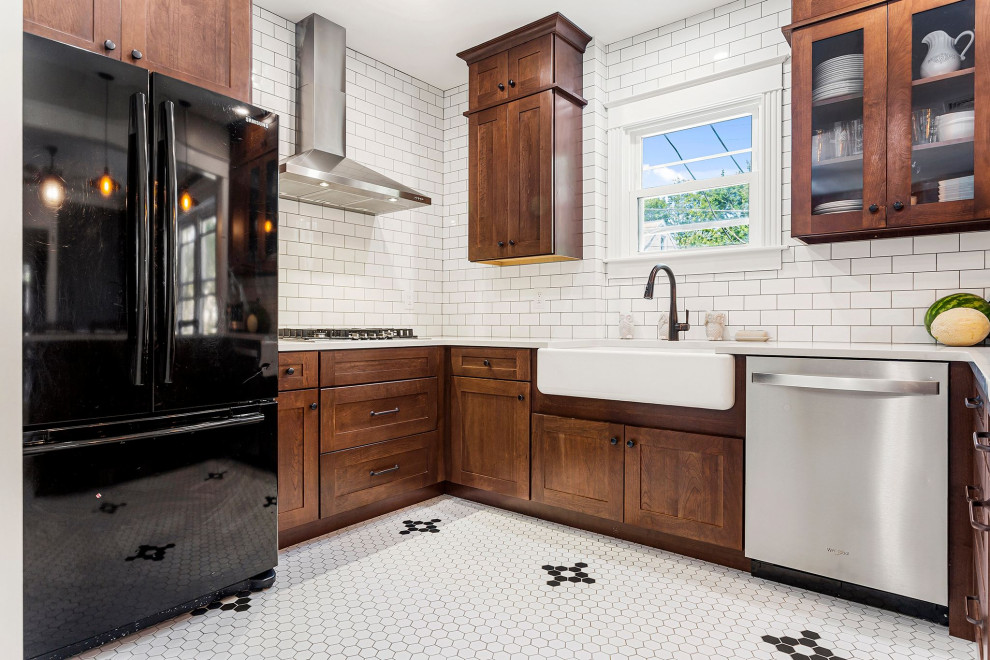 Photo of a large traditional kitchen in Philadelphia with a farmhouse sink, shaker cabinets, brown cabinets, quartz benchtops, white splashback, subway tile splashback, stainless steel appliances, porcelain floors, a peninsula, white floor and white benchtop.