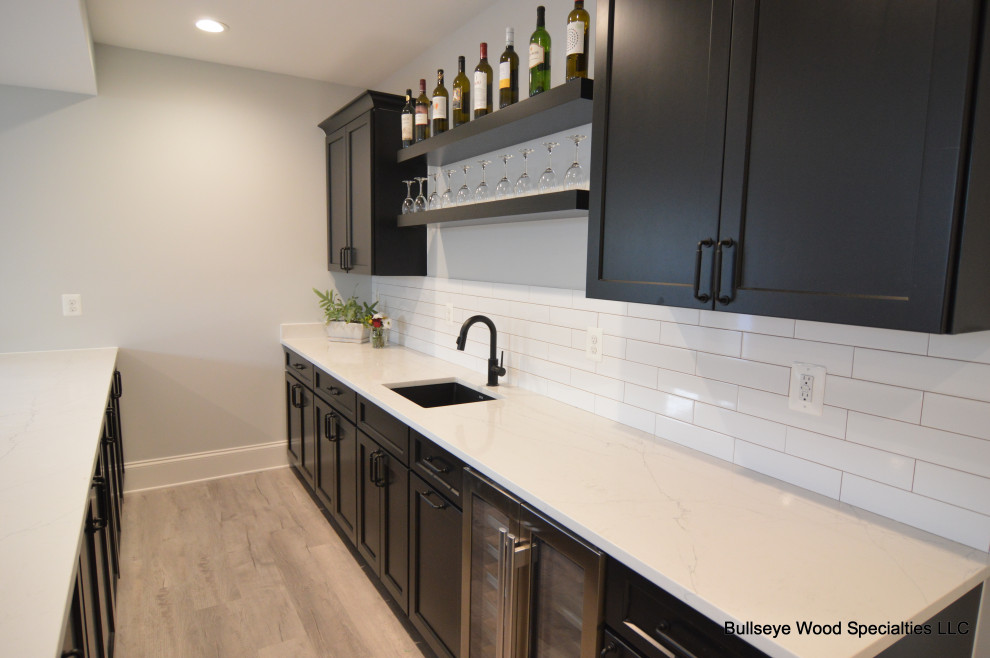 Mid-sized transitional galley seated home bar in DC Metro with an undermount sink, recessed-panel cabinets, blue cabinets, quartz benchtops, white splashback, cement tile splashback, medium hardwood floors, brown floor and grey benchtop.