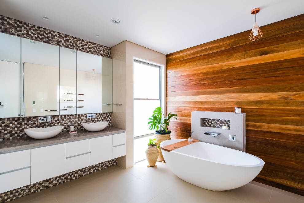 Photo of a contemporary bathroom in Gold Coast - Tweed with flat-panel cabinets, white cabinets, a freestanding tub, multi-coloured tile, mosaic tile, brown walls, a vessel sink, beige floor, grey benchtops, a niche, a double vanity, a floating vanity and wood walls.