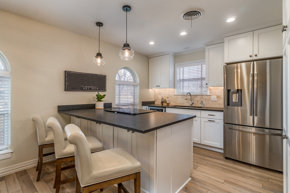 Eat-in kitchen - transitional galley vinyl floor and beige floor eat-in kitchen idea with a double-bowl sink, recessed-panel cabinets, white cabinets, granite countertops, beige backsplash, travertine backsplash, stainless steel appliances, a peninsula and black countertops