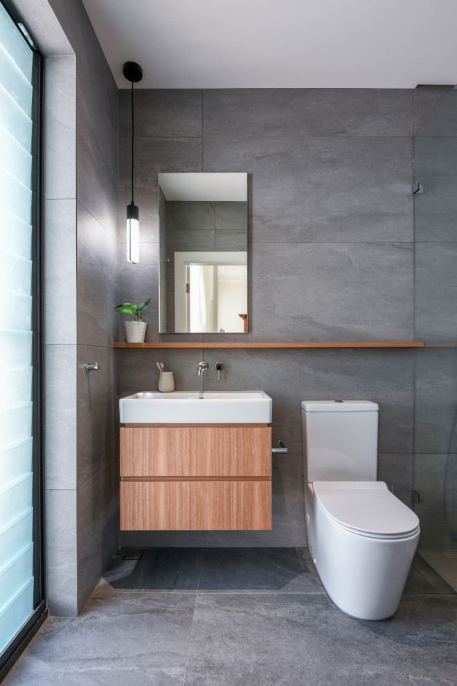 Inspiration for a mid-sized contemporary 3/4 bathroom in Sydney with flat-panel cabinets, medium wood cabinets, gray tile, ceramic tile, ceramic floors, grey floor, an open shower, a curbless shower, a two-piece toilet and a console sink.