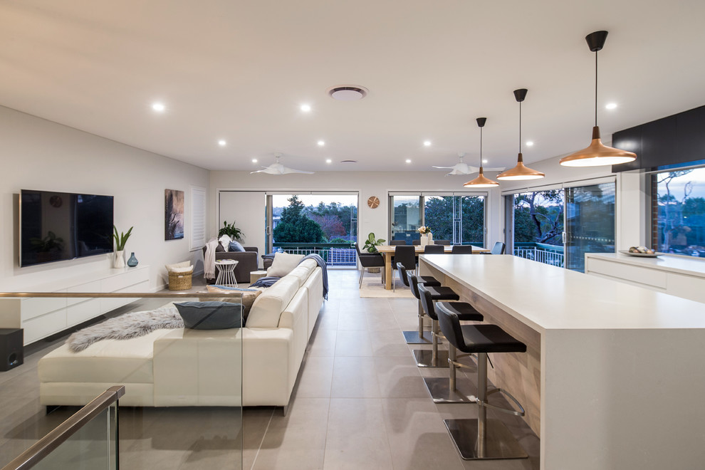 This is an example of a large modern galley open plan kitchen in Sydney with an undermount sink, white cabinets, solid surface benchtops, window splashback, black appliances, porcelain floors and with island.