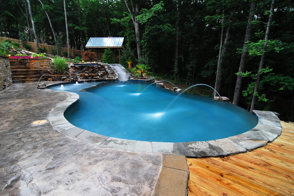 Water slide - large rustic backyard kidney-shaped and stamped concrete infinity water slide idea in Atlanta
