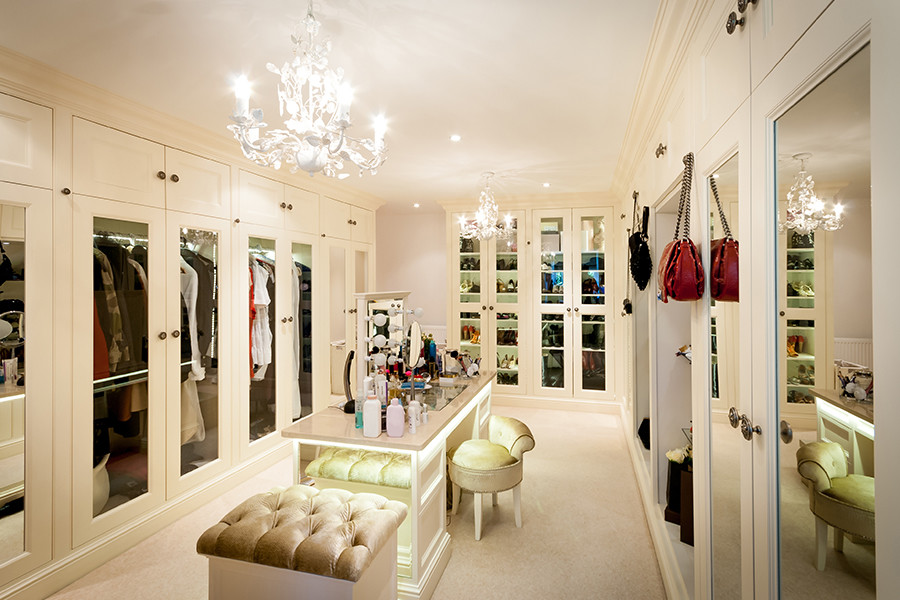 This is an example of an expansive traditional women's dressing room in Surrey with white cabinets and carpet.