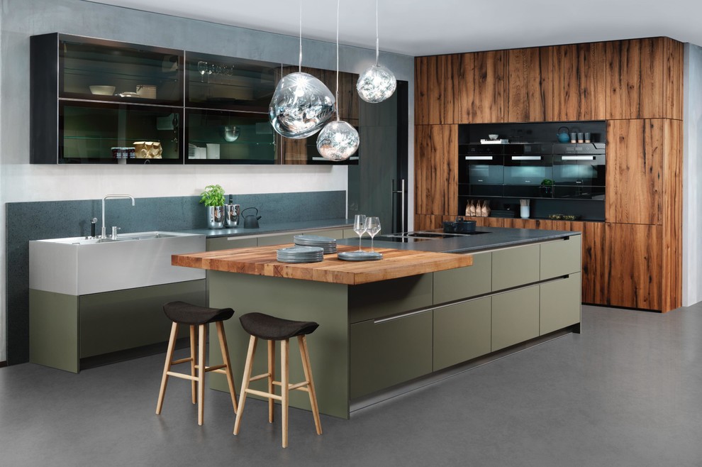 Mid-sized arts and crafts galley open plan kitchen in Miami with a farmhouse sink, flat-panel cabinets, green cabinets, quartz benchtops, grey splashback, black appliances, concrete floors and with island.