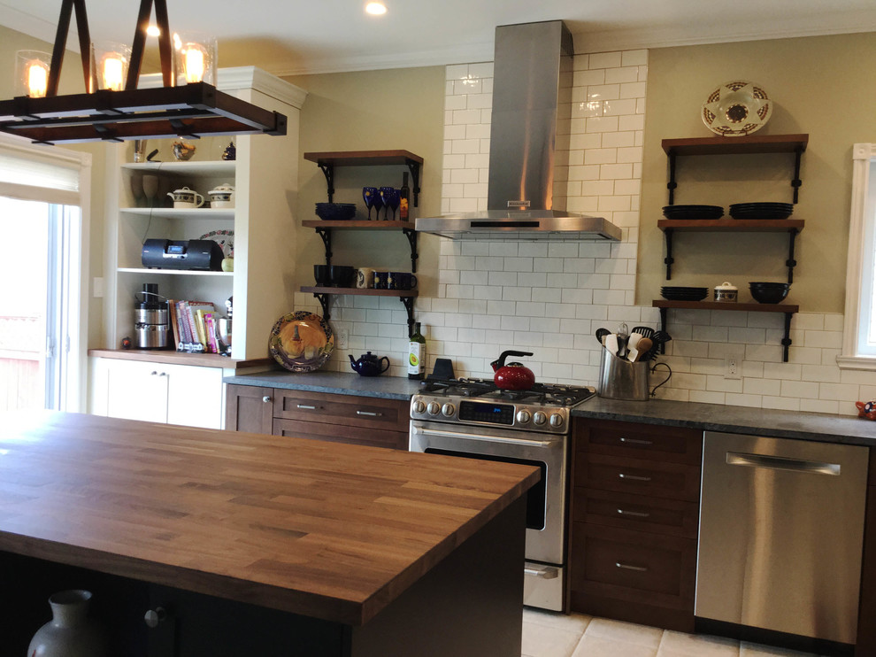 Inspiration for a mid-sized transitional l-shaped kitchen remodel in Ottawa with an undermount sink, shaker cabinets, dark wood cabinets, soapstone countertops, white backsplash, ceramic backsplash, stainless steel appliances and an island