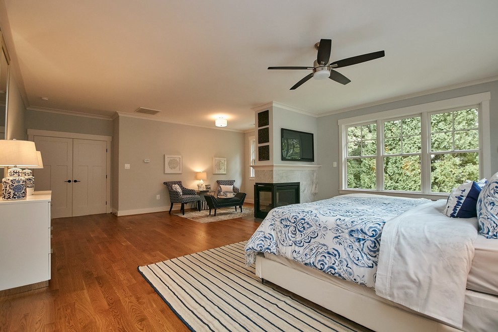 Large country master bedroom in DC Metro with grey walls, medium hardwood floors, a two-sided fireplace, a stone fireplace surround and brown floor.