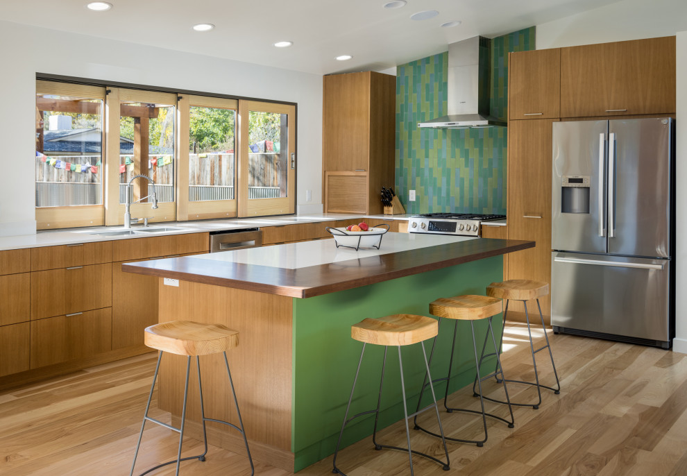 他の地域にあるお手頃価格の中くらいなコンテンポラリースタイルのおしゃれなキッチン (アンダーカウンターシンク、フラットパネル扉のキャビネット、中間色木目調キャビネット、木材カウンター、緑のキッチンパネル、セラミックタイルのキッチンパネル、シルバーの調理設備、淡色無垢フローリング、白いキッチンカウンター、三角天井) の写真