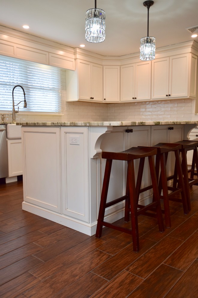 Example of a large transitional u-shaped dark wood floor and brown floor enclosed kitchen design with a farmhouse sink, beaded inset cabinets, white cabinets, granite countertops, beige backsplash, ceramic backsplash, stainless steel appliances, an island and multicolored countertops