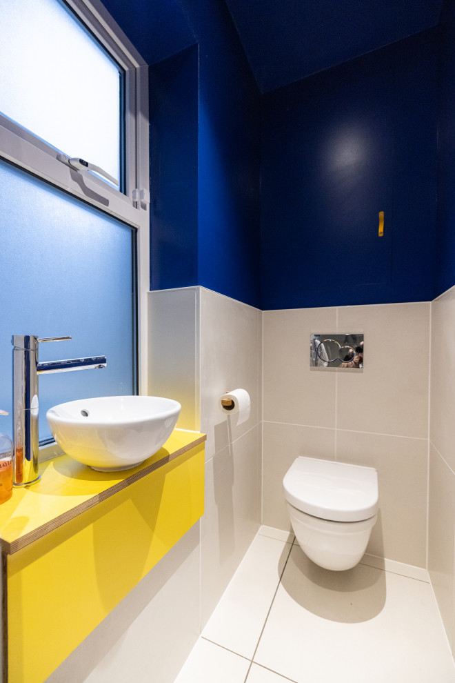 This is an example of a small eclectic 3/4 bathroom in London with yellow cabinets, an alcove shower, a wall-mount toilet, white tile, porcelain tile, white walls, porcelain floors, a drop-in sink, wood benchtops, white floor, a hinged shower door, yellow benchtops, a single vanity and a built-in vanity.