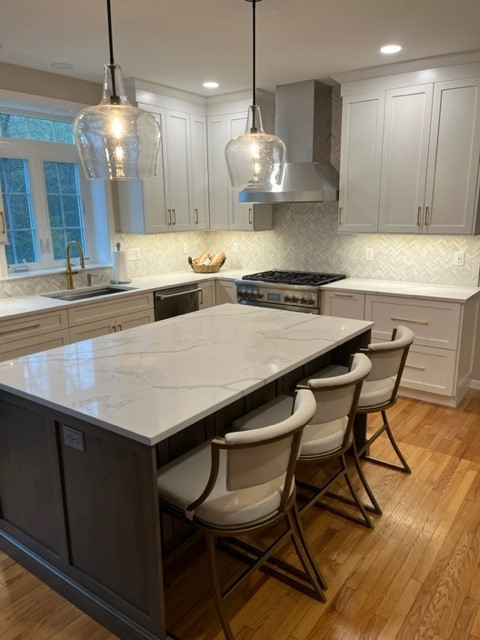 Large transitional l-shaped medium tone wood floor and brown floor eat-in kitchen photo in Boston with an undermount sink, shaker cabinets, white cabinets, quartz countertops, white backsplash, stainless steel appliances, an island and white countertops