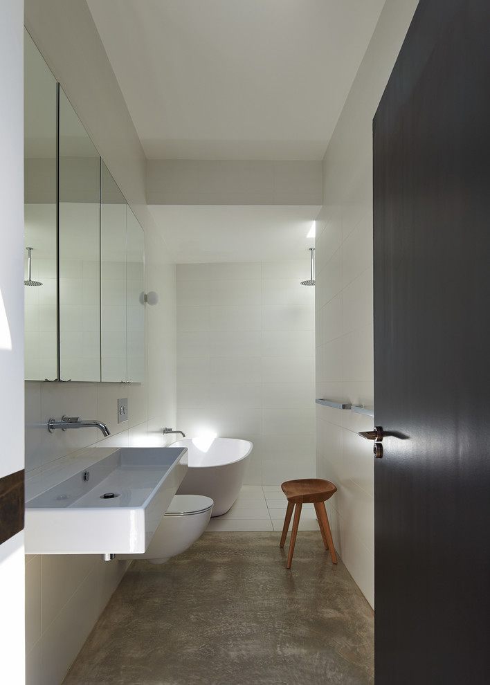 Design ideas for a mid-sized contemporary bathroom in Sydney with recessed-panel cabinets, a freestanding tub, an open shower, a wall-mount toilet, white tile, ceramic tile, white walls, concrete floors and a wall-mount sink.