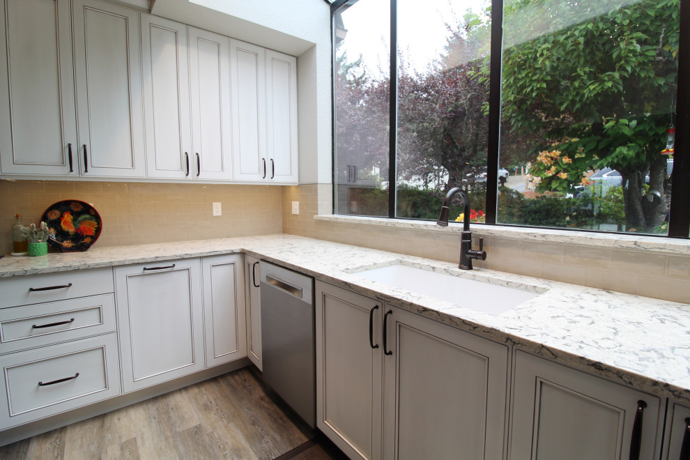 Example of a mid-sized transitional u-shaped vinyl floor, brown floor and vaulted ceiling open concept kitchen design in Seattle with an undermount sink, recessed-panel cabinets, white cabinets, quartz countertops, beige backsplash, subway tile backsplash, stainless steel appliances, an island and multicolored countertops