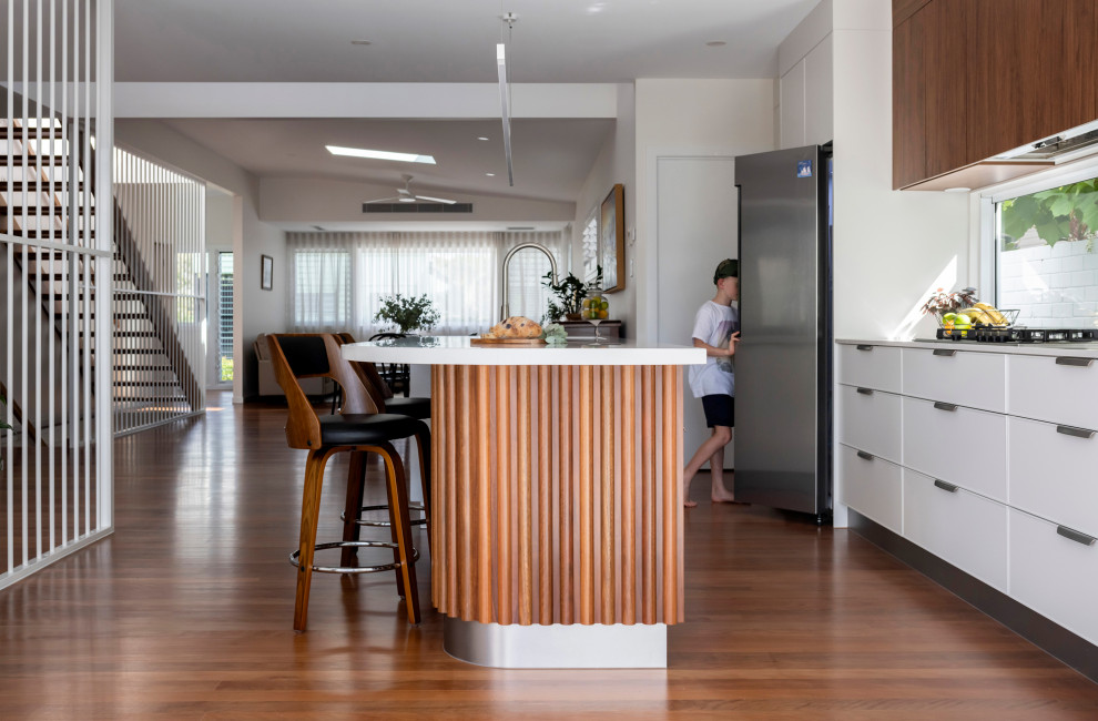 This is an example of a large modern galley eat-in kitchen in Brisbane with an undermount sink, flat-panel cabinets, medium wood cabinets, marble benchtops, window splashback, stainless steel appliances, medium hardwood floors, with island, brown floor and white benchtop.