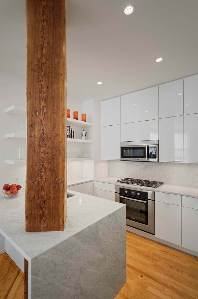 This is an example of a small modern u-shaped eat-in kitchen in New York with an undermount sink, flat-panel cabinets, white cabinets, marble benchtops, white splashback, marble splashback, stainless steel appliances, light hardwood floors, a peninsula and beige floor.