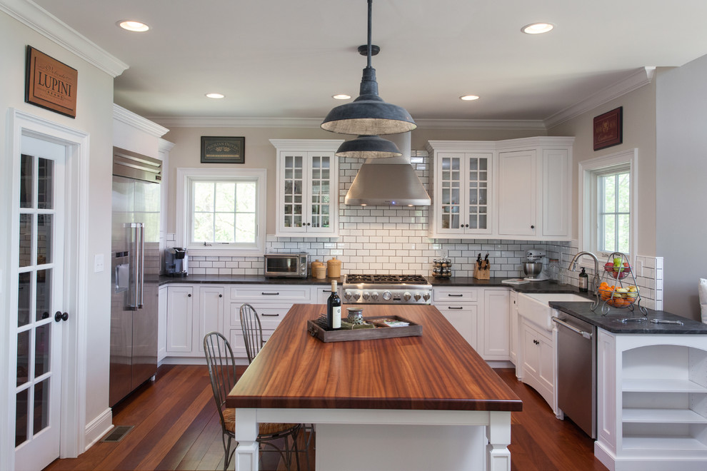 This is an example of a mid-sized traditional u-shaped separate kitchen in Philadelphia with a farmhouse sink, glass-front cabinets, white cabinets, concrete benchtops, white splashback, subway tile splashback, stainless steel appliances, bamboo floors, with island, brown floor and brown benchtop.