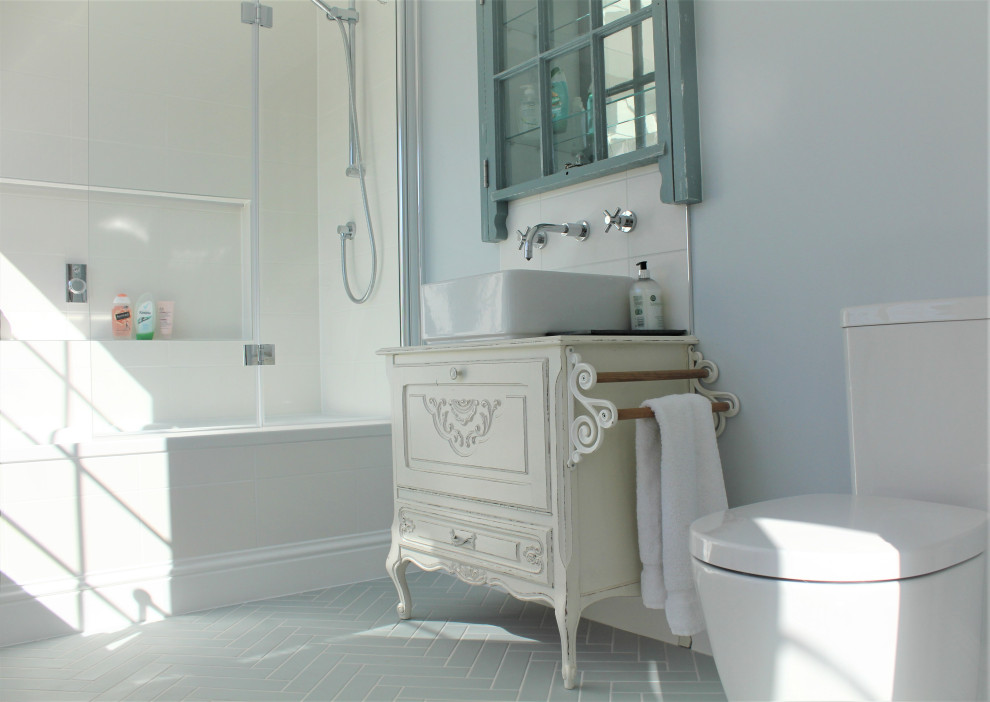 Réalisation d'une salle de bain principale tradition de taille moyenne avec un placard avec porte à panneau surélevé, des portes de placard blanches, une baignoire posée, un combiné douche/baignoire, WC séparés, un carrelage blanc, des carreaux de céramique, un mur bleu, un sol en carrelage de céramique, une vasque, un plan de toilette en verre, un sol bleu, une cabine de douche à porte battante, meuble simple vasque et meuble-lavabo sur pied.