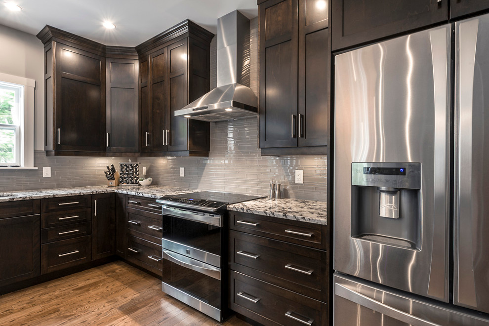 Inspiration for a mid-sized transitional l-shaped medium tone wood floor and brown floor eat-in kitchen remodel with an undermount sink, shaker cabinets, dark wood cabinets, granite countertops, gray backsplash, glass tile backsplash, stainless steel appliances and an island