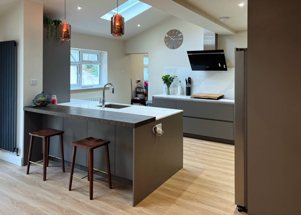 Mid-sized contemporary l-shaped open plan kitchen in London with a single-bowl sink, flat-panel cabinets, grey cabinets, quartzite benchtops, white splashback, stainless steel appliances, with island, beige floor, white benchtop and exposed beam.