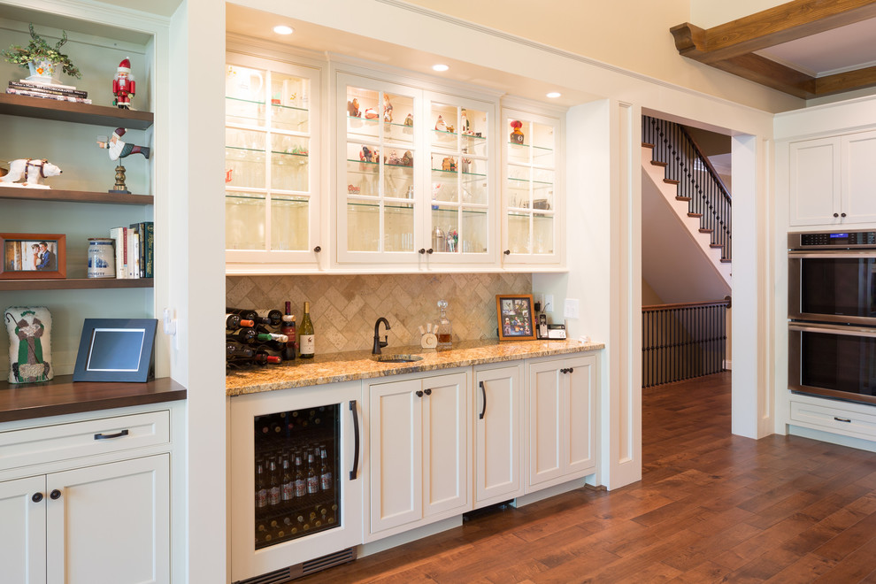 Photo of a large modern galley wet bar in Cincinnati with a drop-in sink, beaded inset cabinets, white cabinets, granite benchtops, multi-coloured splashback, ceramic splashback and light hardwood floors.