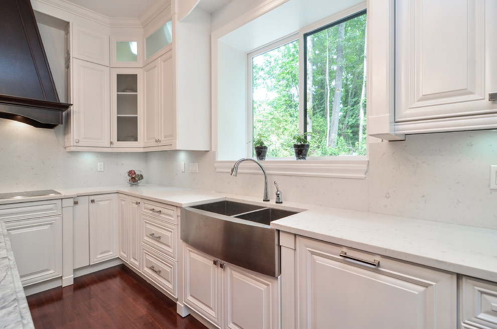 This is an example of a large modern u-shaped eat-in kitchen in Vancouver with raised-panel cabinets, white cabinets, with island, a farmhouse sink, granite benchtops, stainless steel appliances, medium hardwood floors, white splashback and ceramic splashback.