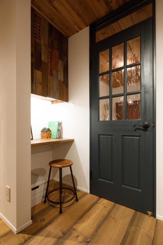 Small industrial home office in Other with white walls, medium hardwood floors, a built-in desk and brown floor.