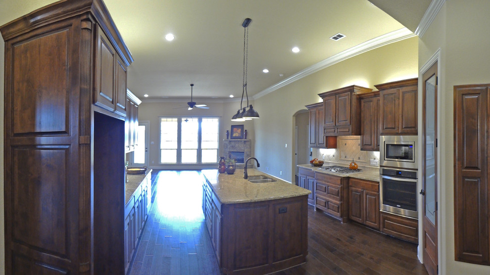 This is an example of a large traditional l-shaped eat-in kitchen in Dallas with an undermount sink, raised-panel cabinets, medium wood cabinets, granite benchtops, beige splashback, stone tile splashback, stainless steel appliances, porcelain floors and with island.