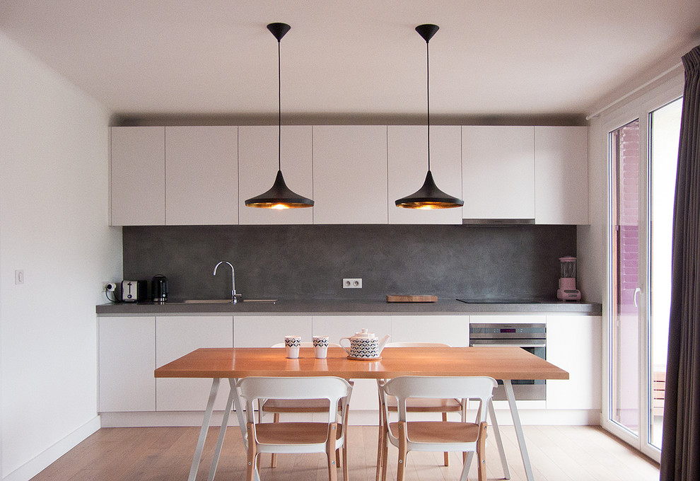 Photo of a mid-sized modern single-wall eat-in kitchen in Lyon with grey splashback, no island, grey cabinets, beaded inset cabinets, light hardwood floors and grey benchtop.