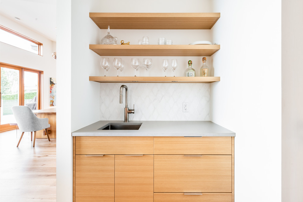Inspiration for a transitional single-wall wet bar in Vancouver with an undermount sink, flat-panel cabinets, light wood cabinets, white splashback, light hardwood floors, beige floor and grey benchtop.