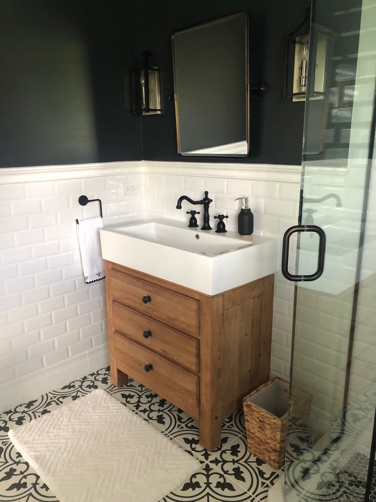Small country bathroom in Chicago with furniture-like cabinets, light wood cabinets, a corner shower, a one-piece toilet, white tile, ceramic tile, black walls, ceramic floors, a trough sink, black floor and a hinged shower door.