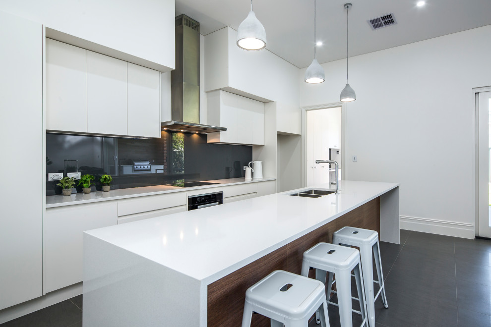Photo of a large modern galley open plan kitchen in Adelaide with an undermount sink, flat-panel cabinets, white cabinets, quartz benchtops, grey splashback, glass sheet splashback, black appliances, porcelain floors, with island, grey floor and white benchtop.