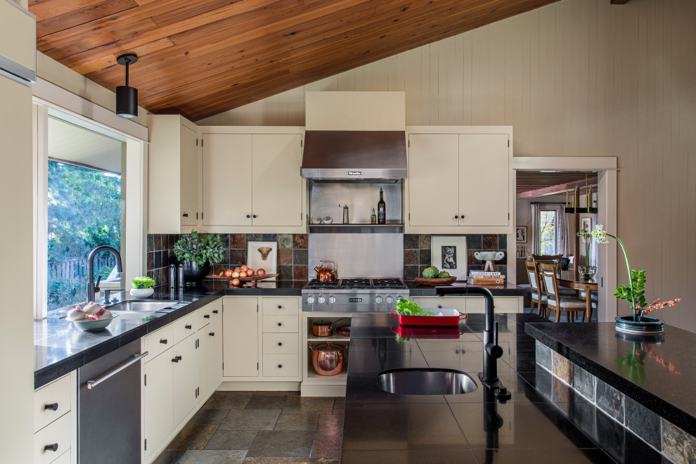 Large midcentury l-shaped kitchen in Portland with a double-bowl sink, flat-panel cabinets, beige cabinets, granite benchtops, multi-coloured splashback, slate splashback, stainless steel appliances, slate floors, with island, brown floor, black benchtop and wood.