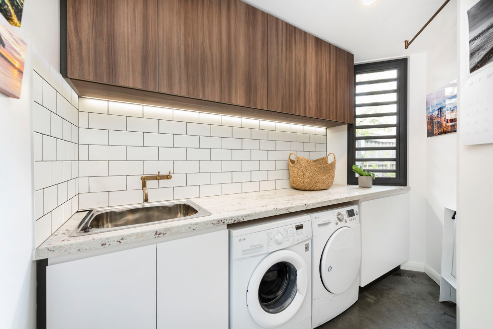 Photo of a mid-sized contemporary galley dedicated laundry room in Melbourne with a drop-in sink, flat-panel cabinets, medium wood cabinets, granite benchtops, white walls, concrete floors, a side-by-side washer and dryer, grey floor and white benchtop.