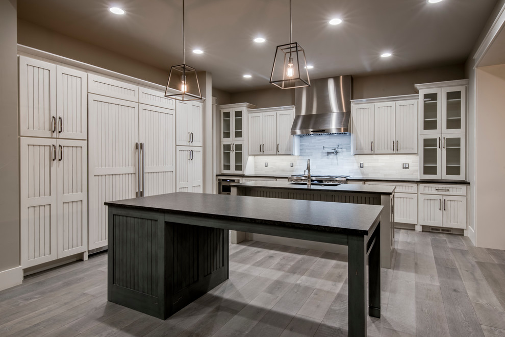 This is an example of a large classic single-wall kitchen in Denver with a submerged sink, shaker cabinets, distressed cabinets, granite worktops, grey splashback, limestone splashback, stainless steel appliances, light hardwood flooring, multiple islands, grey floors and black worktops.
