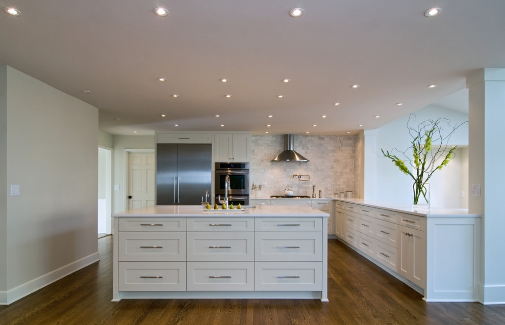 Large transitional l-shaped open plan kitchen in Portland with an undermount sink, shaker cabinets, white cabinets, quartz benchtops, white splashback, marble splashback, stainless steel appliances, medium hardwood floors, with island and brown floor.