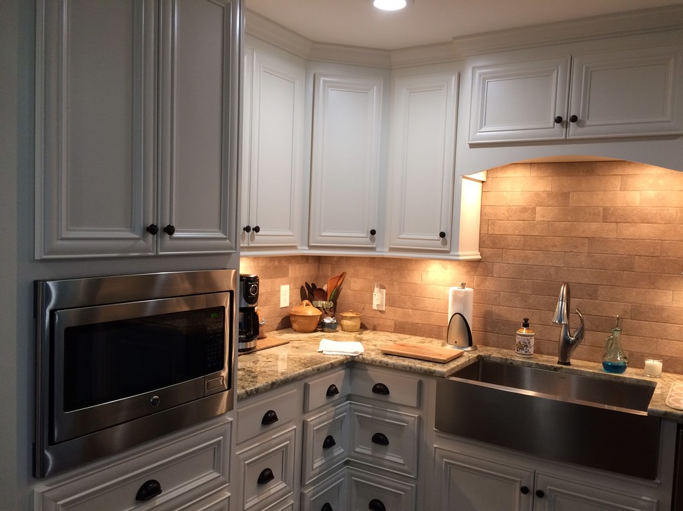 Example of a large transitional l-shaped brown floor eat-in kitchen design in Birmingham with a farmhouse sink, recessed-panel cabinets, white cabinets, beige backsplash, stainless steel appliances and an island