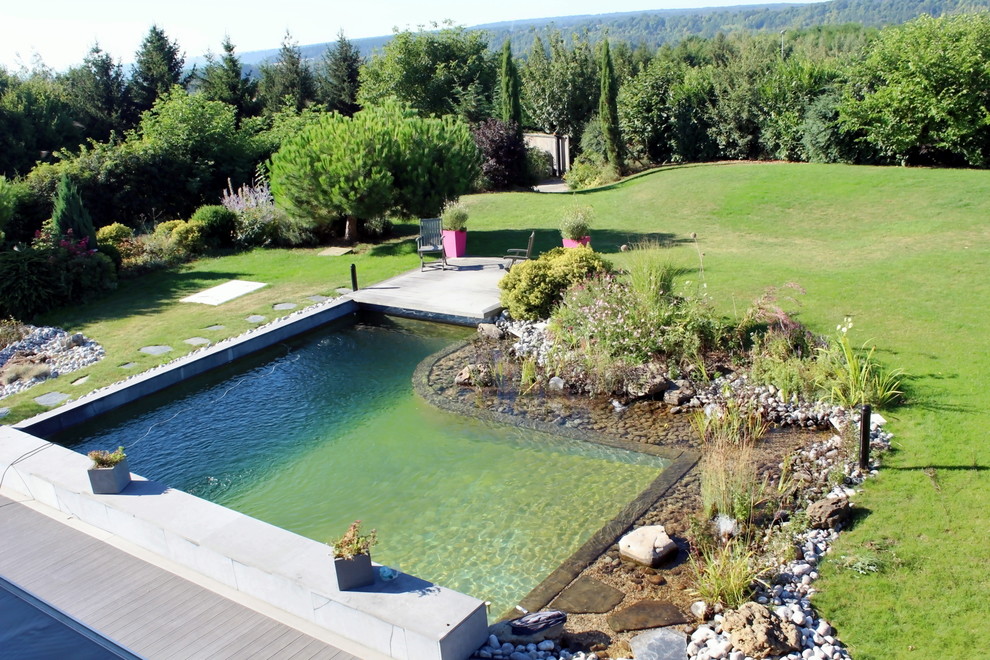 This is an example of a mid-sized country backyard custom-shaped natural pool in Paris with a hot tub and gravel.