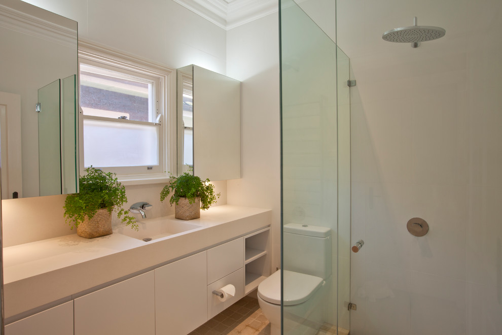 Large transitional kids bathroom in Sydney with an integrated sink, flat-panel cabinets, white cabinets, solid surface benchtops, a corner shower, a one-piece toilet, beige tile, stone tile and white walls.